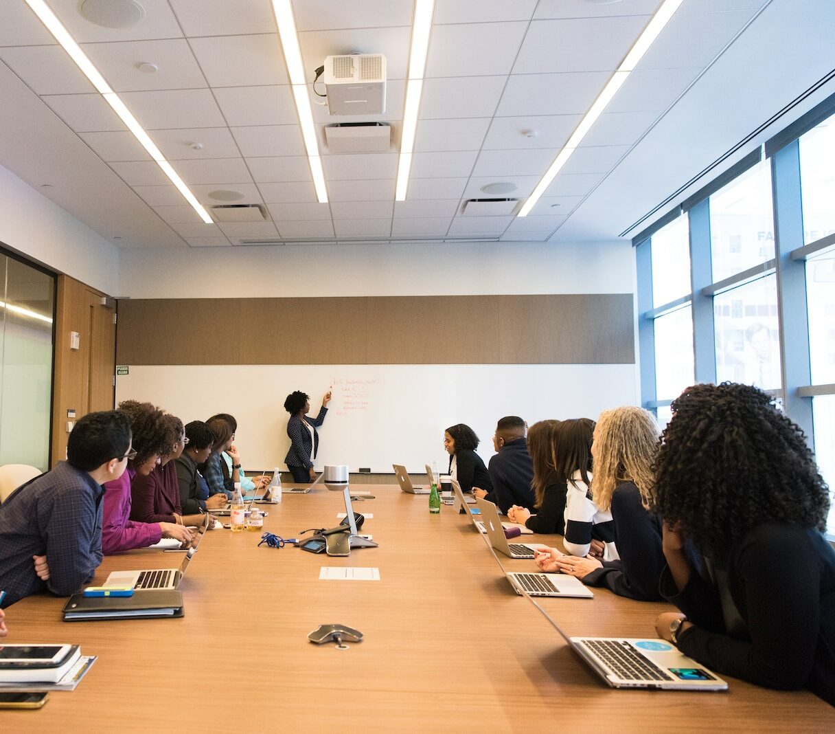 people on conference table looking at talking woman