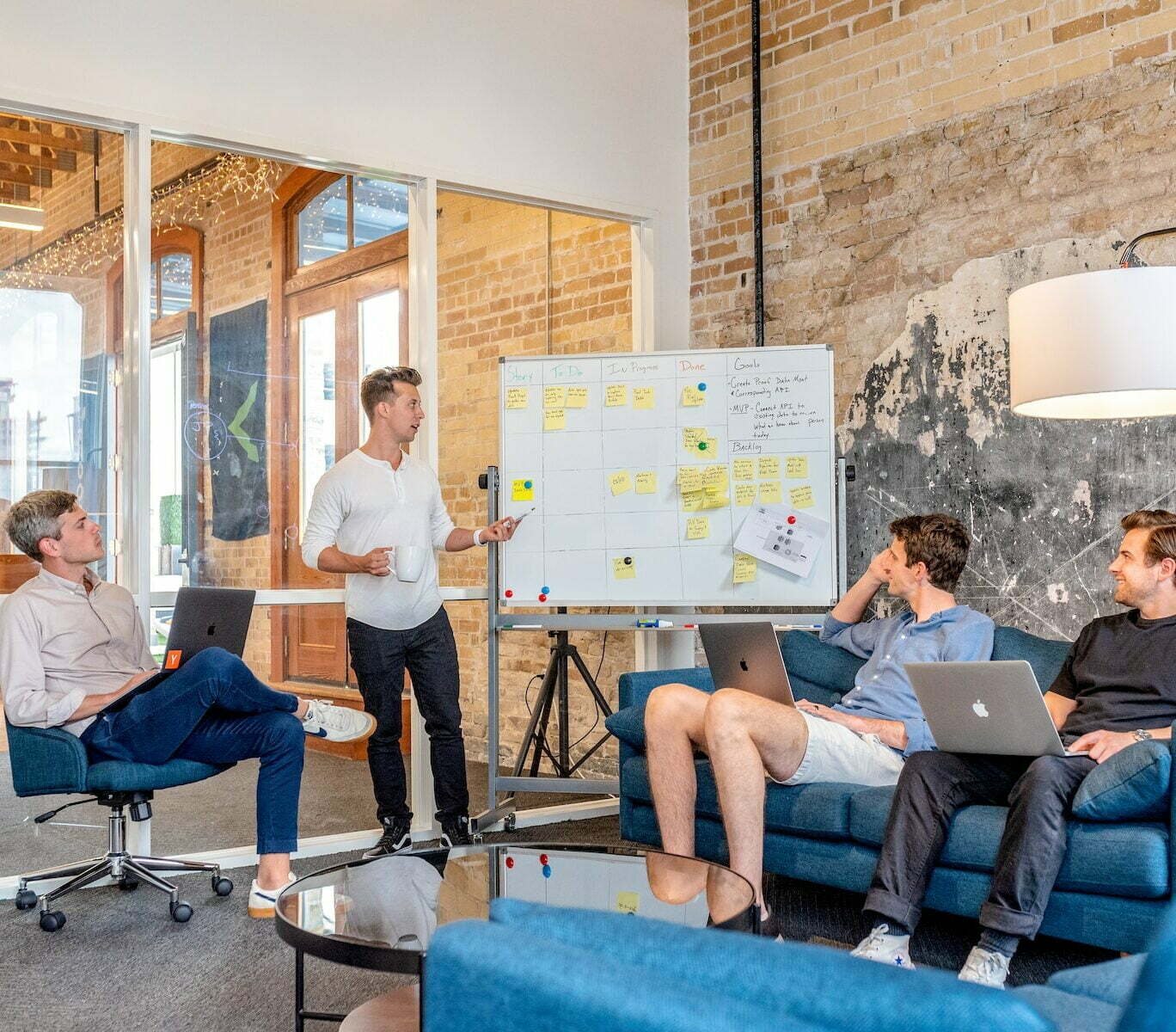 three men sitting while using laptops and watching man beside whiteboard